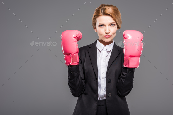 serious businesswoman posing in suit and pink boxing gloves, isolated on grey