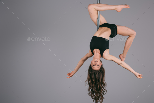 upside down of beautiful sporty girl exercising with pole and looking at  camera on grey Stock Photo by LightFieldStudios