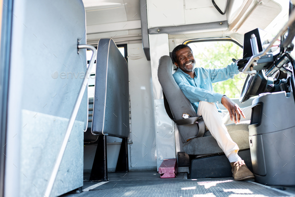 happy mature african american bus driver looking at camera while sitting inside bus