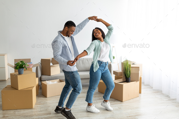 Happy affectionate black spouses dancing in their new apartment among cardboard boxes on moving day - Stock Photo - Images