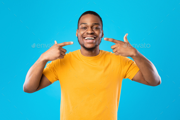 Black Man Pointing Fingers At His Smile Over Blue Background