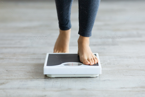 Unrecognizable young Indian woman stepping on scales to measure her weight at home, closeup of feet