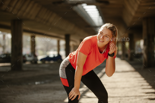 Fitness girl with headphones in ears, plays music on her phone and starts running around the city.