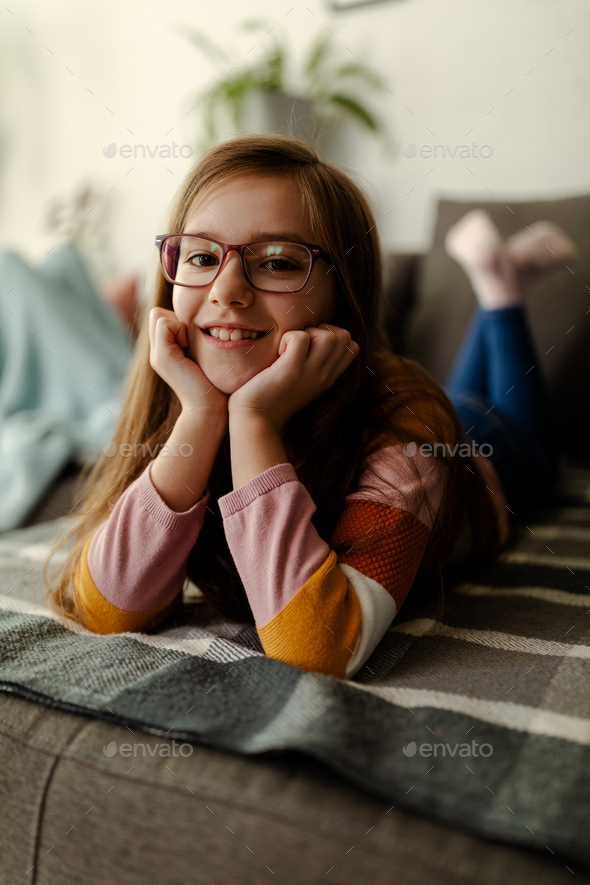 Close up photo of cute smiling little girl, laying on stomach at couch, chilling and relaxing.