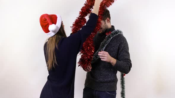 A woman decorating a man with tinsel alt
