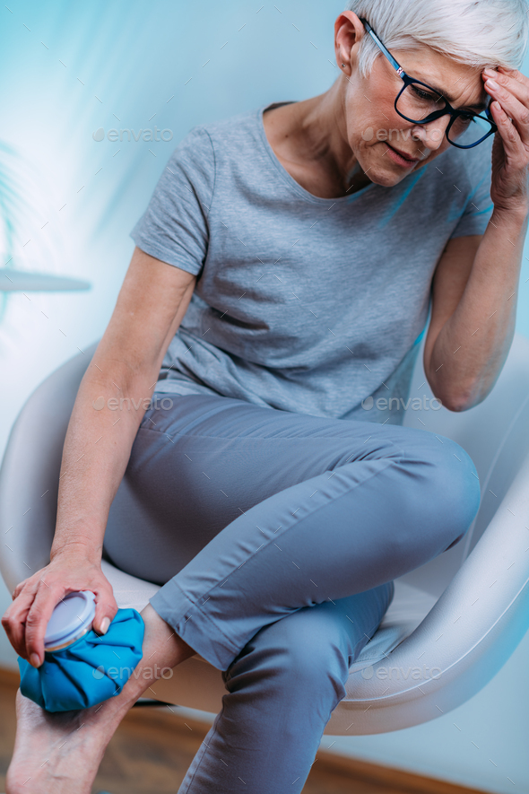 Ankle Pain Treatment. Senior Woman Holding Ice Bag Compress on a Painful Ankle Joint.