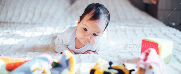 Cute little three month old baby girl, playing at home in bed in bedroom, soft back light in front - Stock Photo - Images