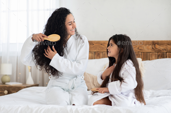 Fair-haired brunette mother and little daughter brushing hair - Stock Photo - Images