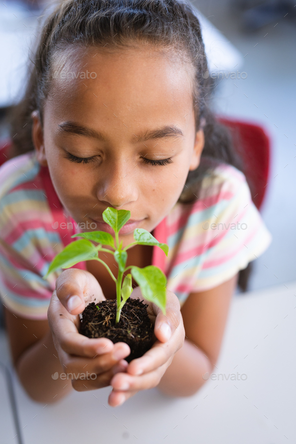 Close up of african american girl with eyes closed holding a plant seedling in the class at school - Stock Photo - Images