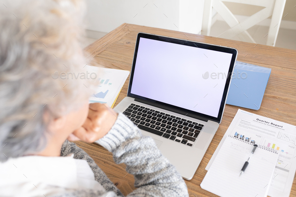 Mixed race senior woman sitting at table making video call using laptop - Stock Photo - Images