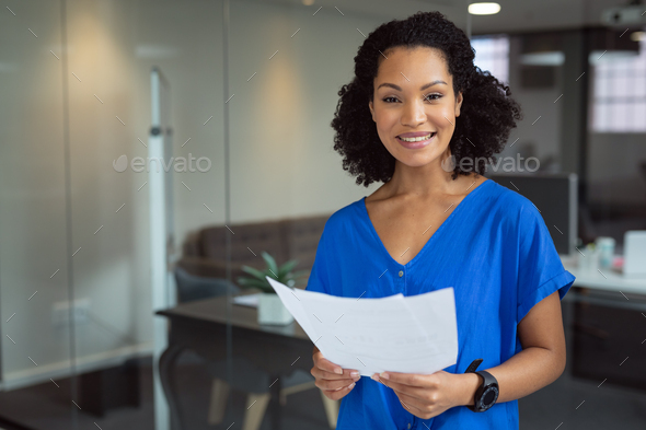 Portrait of smiling african american businesswoman holding paperwork standing in office - Stock Photo - Images