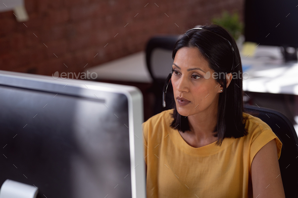 Caucasian businesswoman wearing phone headset sitting in office using computer and concentrating - Stock Photo - Images