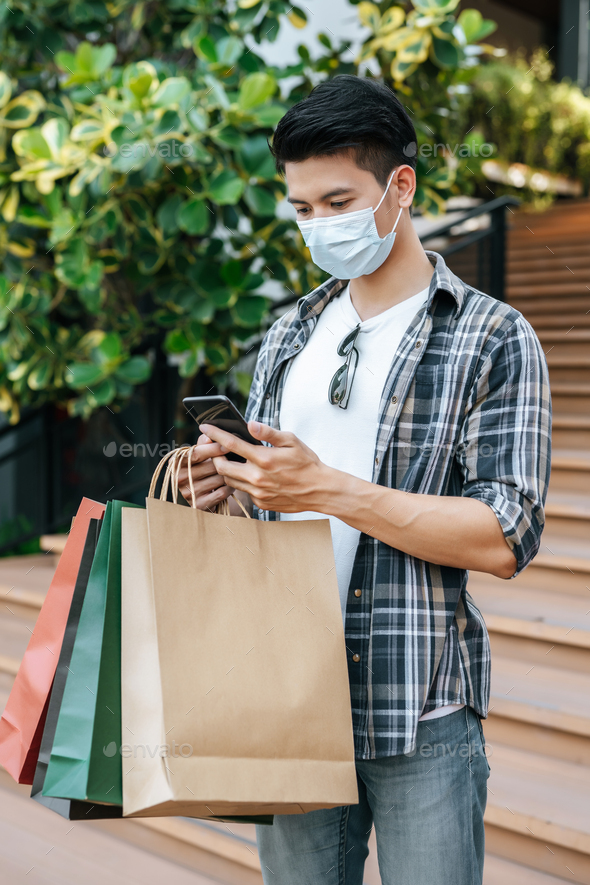 Handsome man with shopping bag and smartphone at shopping mall