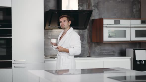 Handsome Man Having Breakfast in Bathrobe Drinking Coffee at Home in Kitchen alt