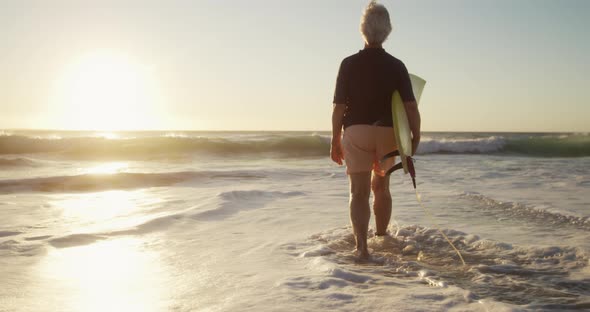 Senior man walking with surfboard at the beach alt
