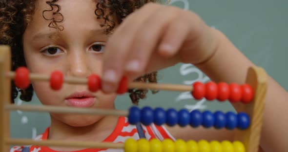 Front view of mixed-race schoolgirl learning mathematics with abacus in a classroom at school 4k alt