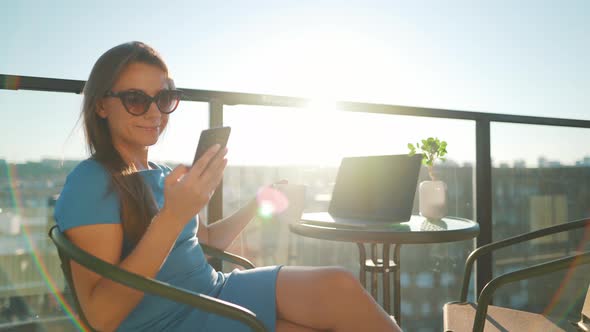 Woman Using Smartphone on the Balcony Against the Backdrop of the Sunset. Outdoor Home Office alt