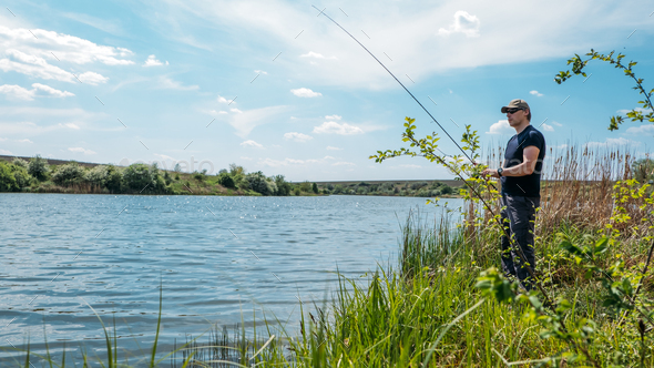 Fisherman with spinning rod on nature background. Angler man with fishing  spinning or casting rod by Stock Photo by IrynaKhabliuk