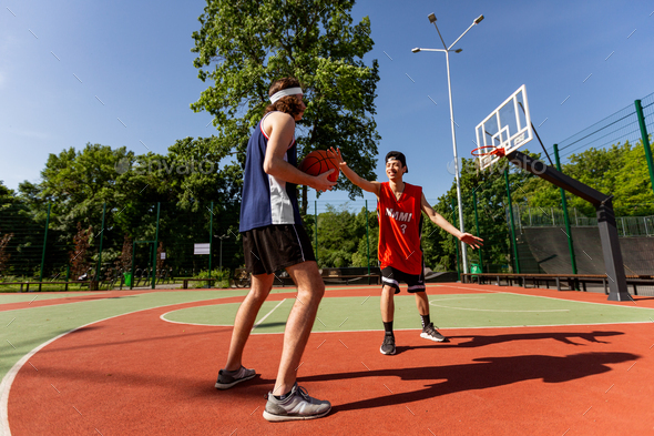 Two millennial sportsmen playing basketball match at outdoor playground, blank space - Stock Photo - Images
