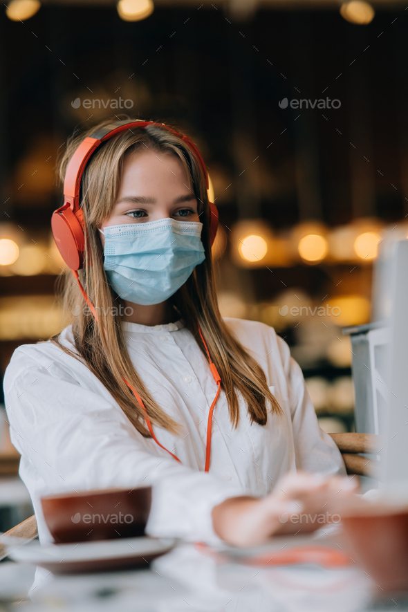 A girl sitting in a coffee shop with headphones. Coronavirus outbreak - Stock Photo - Images