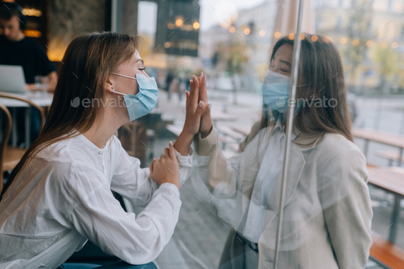 Two women in protective masks opposite each other, window between them - Stock Photo - Images