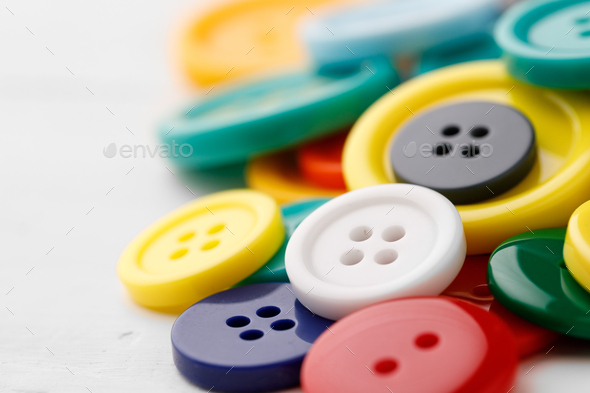 A pile of colorful buttons on a white surface. Buttons colored