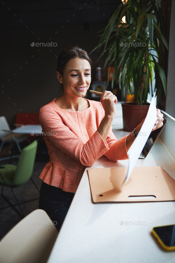 Young attractive Caucasian female founder of company is looking through the documents in the co - Stock Photo - Images