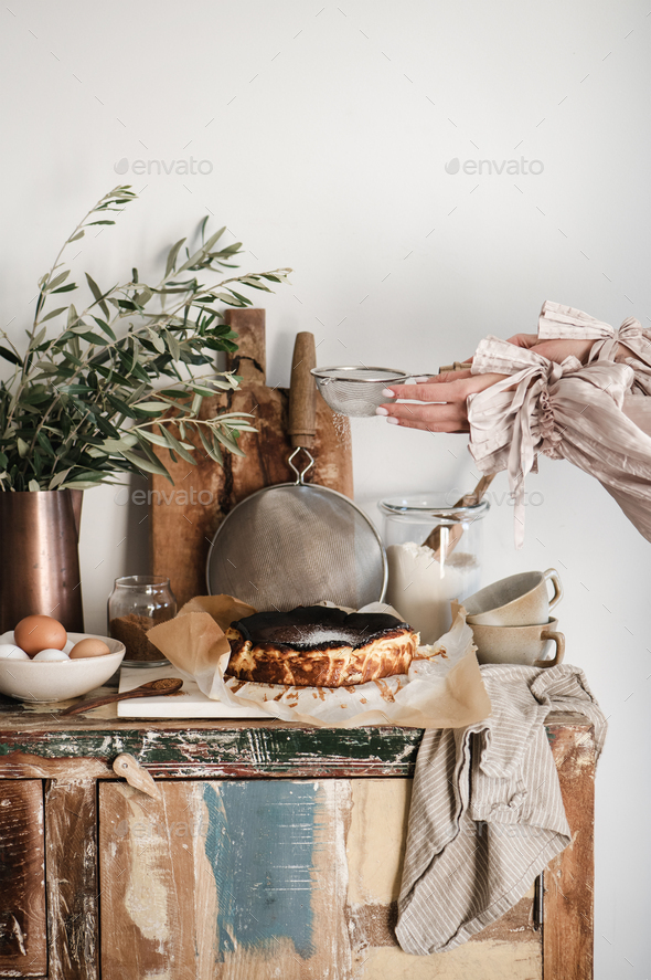 Female hands sprinkling sugar powder over San Sebastian cheesecake - Stock Photo - Images