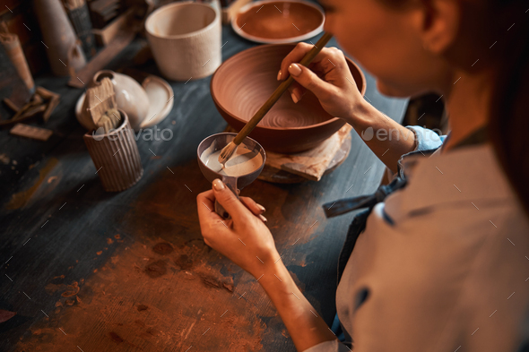 Beautiful elegant woman designer in apron during process making tableware in pottery workshop