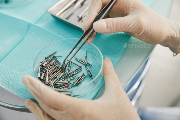 Doctor releasing bur from tweezers to others in glass tray