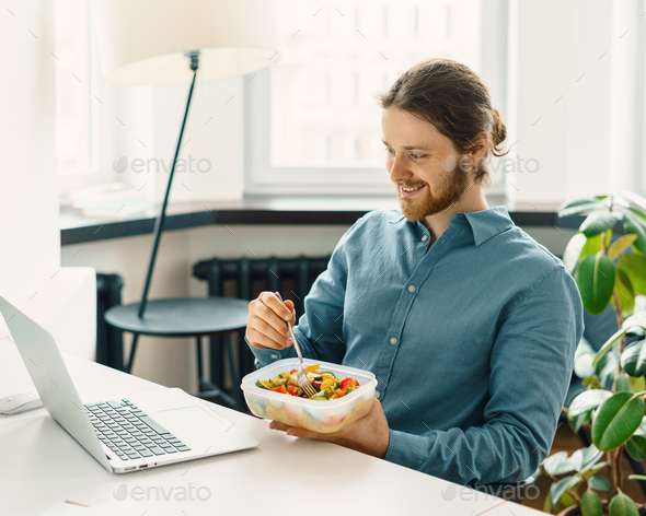 Sitisfied male employee eating vegetarian food at work - Stock Photo - Images