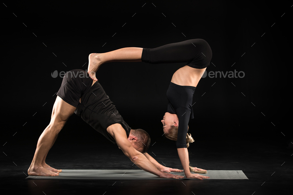 Couple performing acroyoga double down dog pose on yoga mat isolated on black