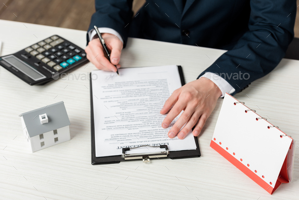 cropped view of realtor signing lease agreement near blank calendar, calculator and house model - Stock Photo - Images