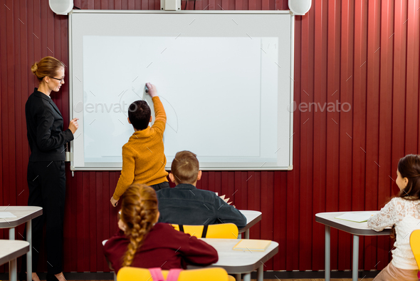 back view of boy writing on interactive whiteboard during lesson