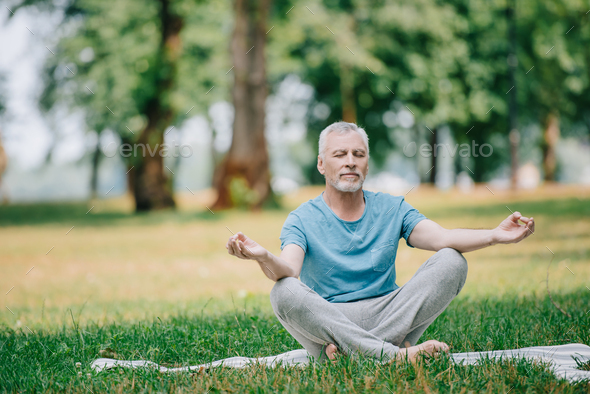 handsome mature man meditating while sitting in lotus pose in park Stock  Photo by LightFieldStudios