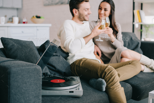 happy young couple listening music with vinyl record player and drinking wine at home