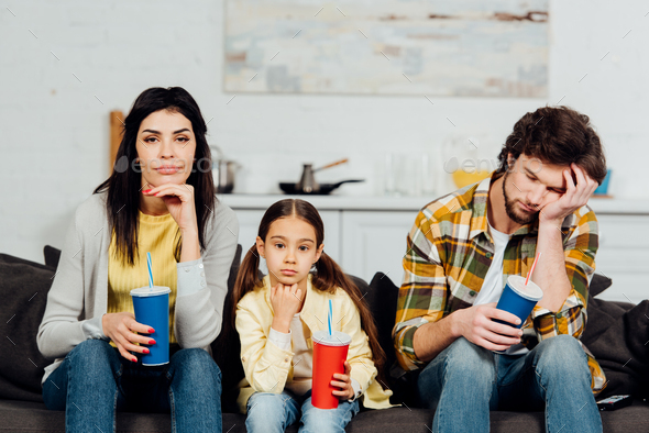 bored family holding disposable cups while watching movie at home