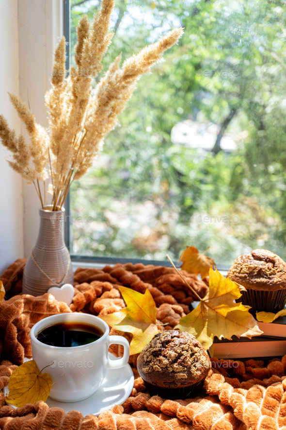 Coffee cup, books, cakes, warm plaid and autumnal leaves on a window sill in autumn