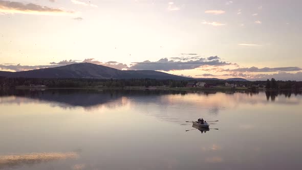 Group of friends rowing a boat in a calm lake during midnight sun in Lapland. alt