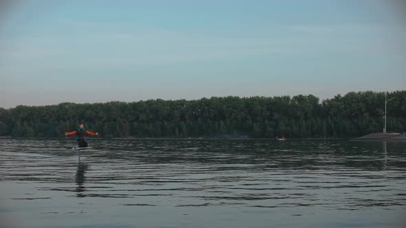 Man Riding a Hydrofoil Surfboard on Large Lake at Golden Sunset Sitting on Knees alt