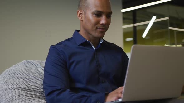 Smiling mixed race businessman sitting at desk using laptop in office alt