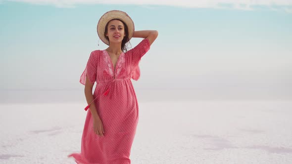 Joyful Freedom Woman in Blowing Pink Dress and Hat Standing on White Endless Salty Beach Like Desert alt