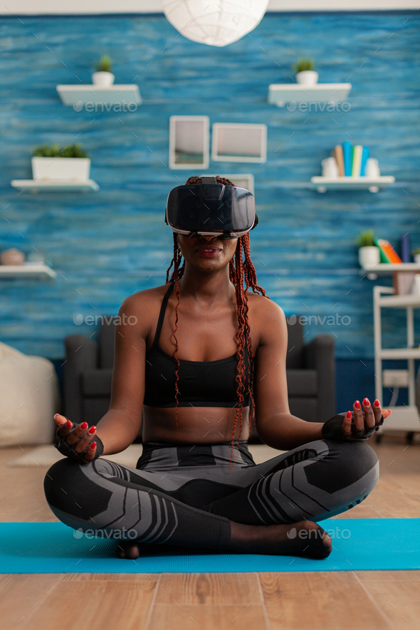Black woman experiencing virtual reality training body and mind meditating in lotus pose