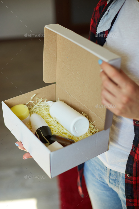 Brunette woman opening, hold in hand online order parcel box with cosmetics at home - Stock Photo - Images