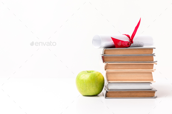 Apple near pile of books with diploma on top isolated on white