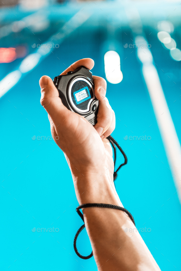 cropped view of swim trainer with stopwatch standing at competition swimming pool