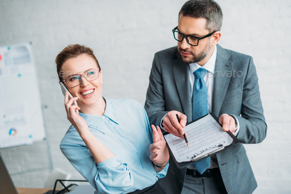 businessman asking his colleague to sign document while she talking by phone and annoying him