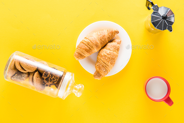 Top view of chocolate chip cookies and tasty croissants with coffee on yellow