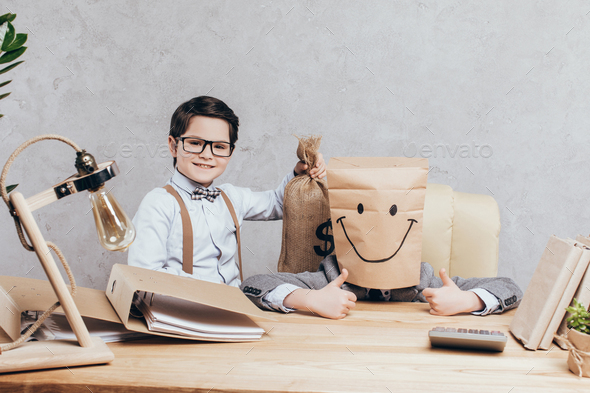 smiling boy with money bag looking at camera and friend with paper bag on head showing thumbs up