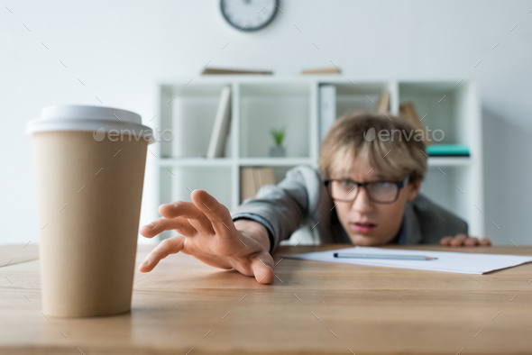 Businessman lying on a table in the office and reaching for coffee in ...